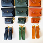 Load image into Gallery viewer, Collection of small leather pouches in various colors with matching straps on a white background.
