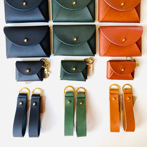 Collection of small leather pouches in various colors with matching straps on a white background.