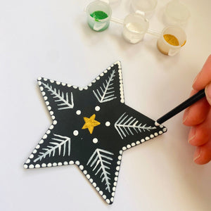 Hand painting a black star with white patterns on a white surface.
