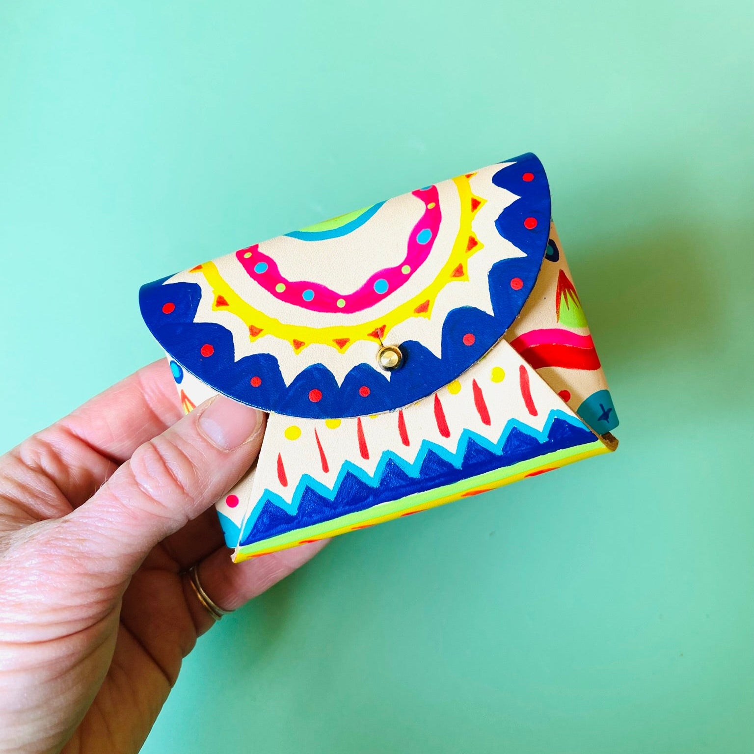 Colorful purse with geometric pattern held by a hand against a light green background