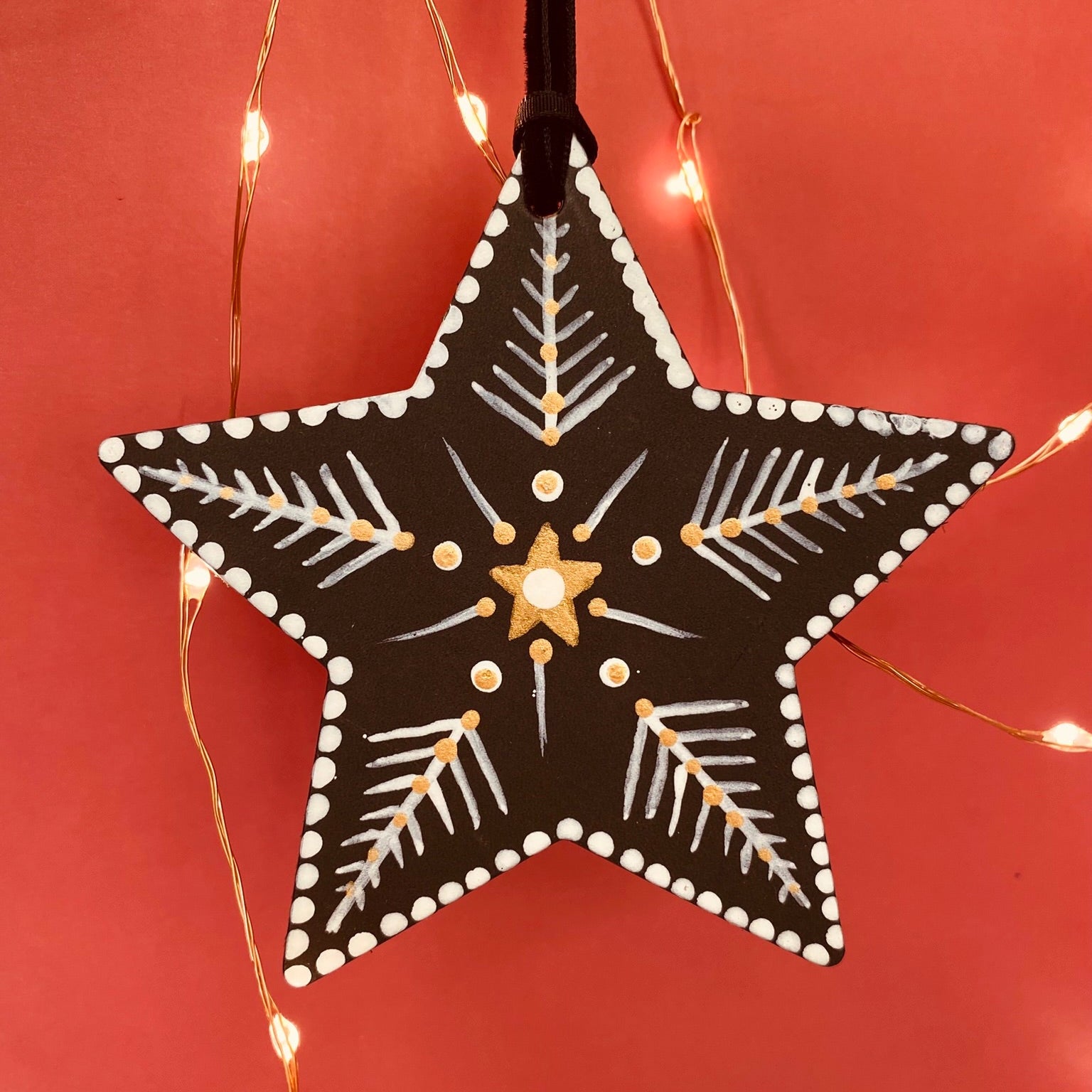 Decorative star ornament with white snowflake patterns and a gold center, hanging against a warm-toned background with string lights.
