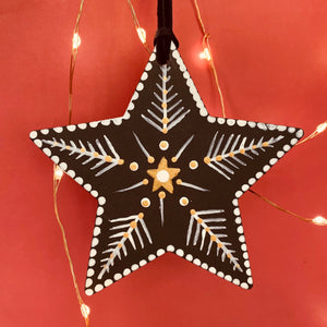 Decorative star ornament with white snowflake patterns and a gold center, hanging against a warm-toned background with string lights.