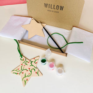 Wooden star ornament with paint supplies and 'Willow' branded box on a red background