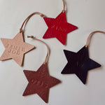 Load image into Gallery viewer, Four embossed star-shaped hanging ornaments in beige, red, brown, and black, each with a leather loop and personalized name or text, arranged on a plain light background.
