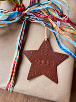 Load image into Gallery viewer, A brown embossed star-shaped ornament with the name 'OTIS' and leaf details, hanging from a colorful paper ribbon on a kraft paper wrapped gift box.
